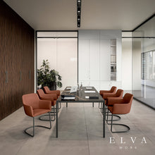 Load image into Gallery viewer, A modern meeting room setup featuring a dark rectangular conference table surrounded by six Elva desk chairs with curved chrome bases. The room has a minimalist design with a dark wood-paneled wall on the left, white cabinets in the background, and a concrete floor.